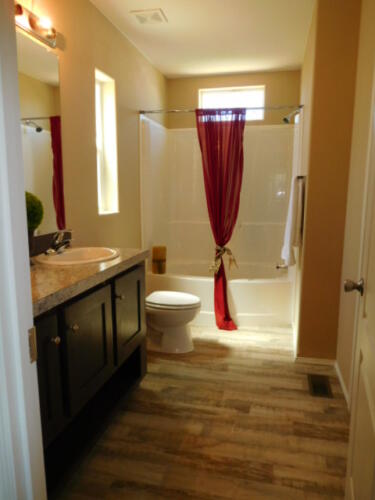 A bathroom with wood floors and a red curtain.